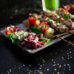 A plate of grilled skewers with vibrant salad and drink, perfect for a summer meal.