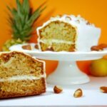 Sliced pineapple and almond cake displayed on a cake stand with vibrant orange background.