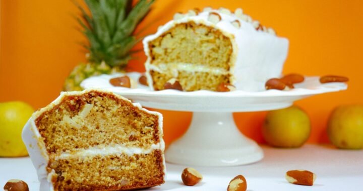 Sliced pineapple and almond cake displayed on a cake stand with vibrant orange background.