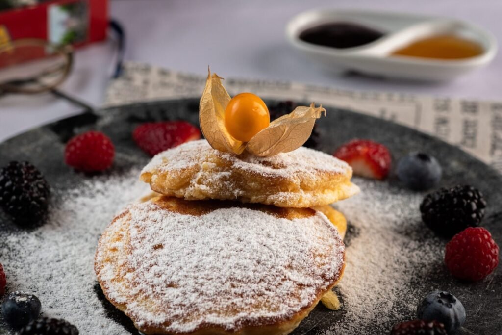 A mouthwatering stack of pancakes dusted with powdered sugar, topped with berries and physalis.
