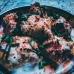 Close-up of traditional Indian dahi vada garnished with yogurt, herbs, and spices.