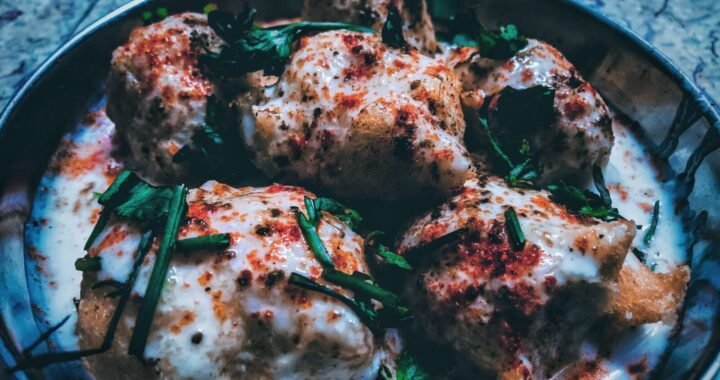 Close-up of traditional Indian dahi vada garnished with yogurt, herbs, and spices.