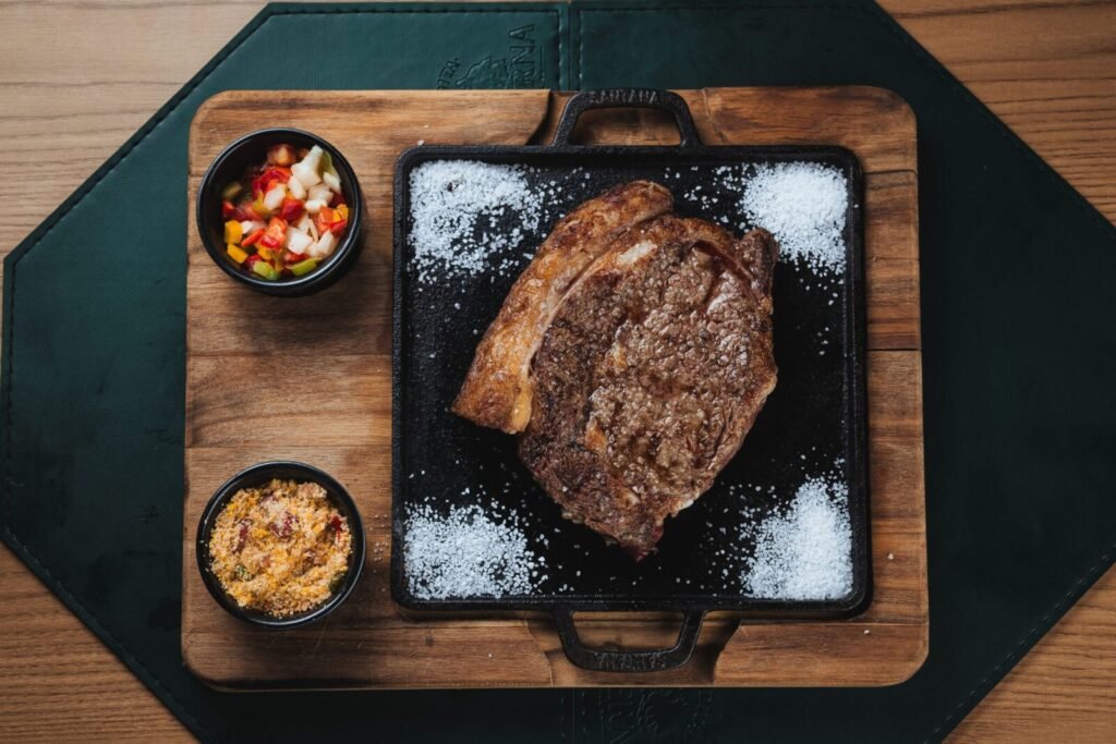 Delicious grilled ribeye steak with colorful salsa and farofa served on a wooden board.