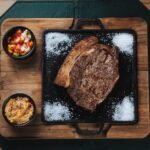 Delicious grilled ribeye steak with colorful salsa and farofa served on a wooden board.