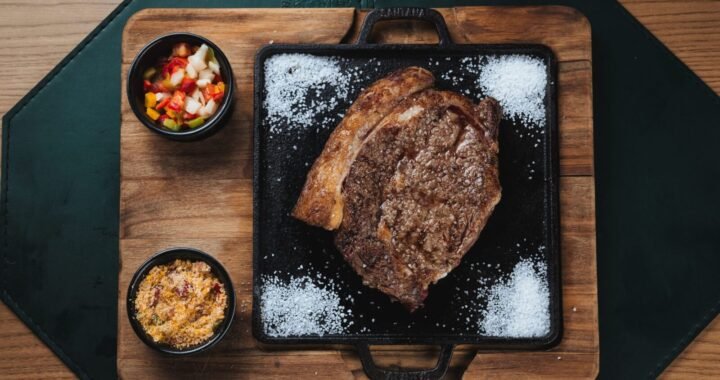 Delicious grilled ribeye steak with colorful salsa and farofa served on a wooden board.