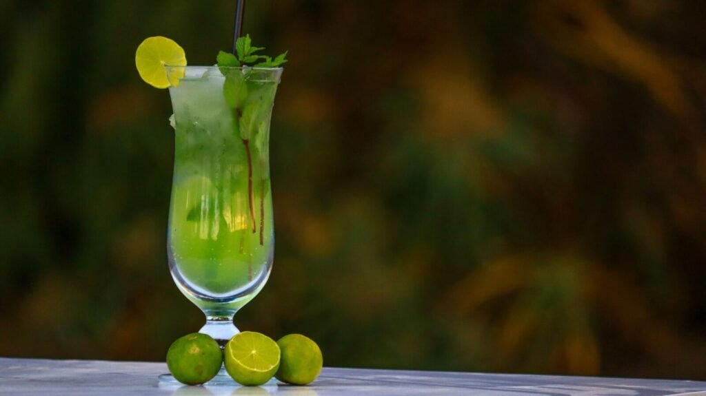Tall glass of lime mint cooler with ice cubes and garnishes, served on a table.