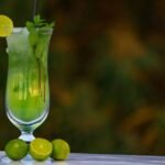 Tall glass of lime mint cooler with ice cubes and garnishes, served on a table.