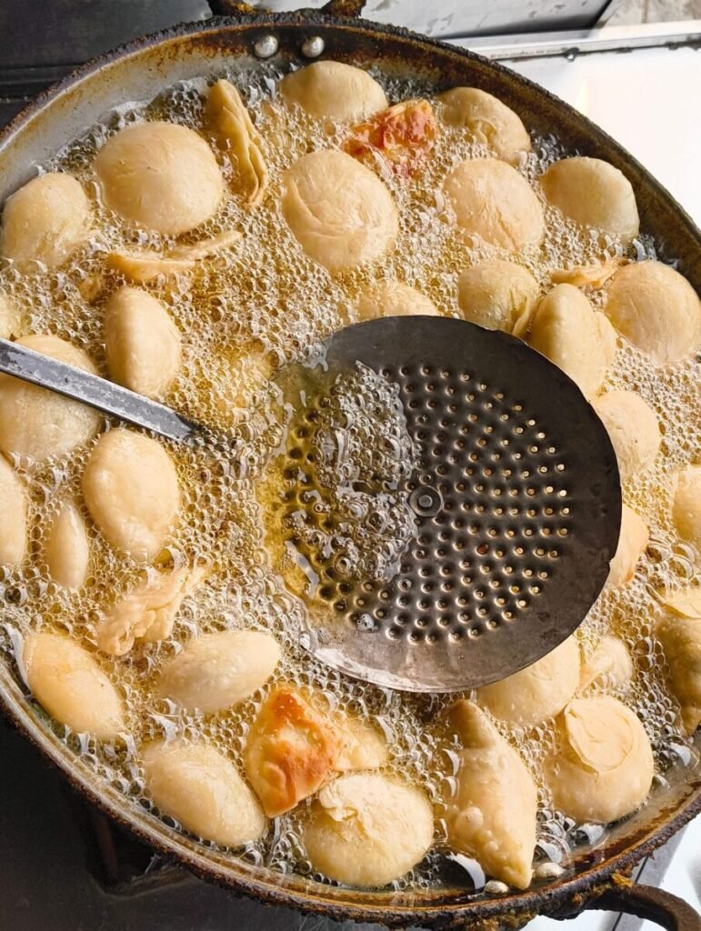 Top view of dumplings frying in oil with perforated ladle. Perfect for culinary themes.