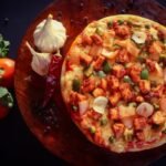 Close-up of homemade pizza topped with vegetables and cheese on a rustic wooden board.