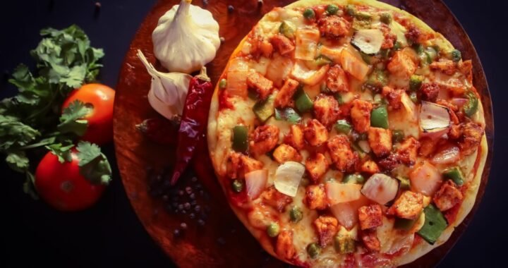 Close-up of homemade pizza topped with vegetables and cheese on a rustic wooden board.