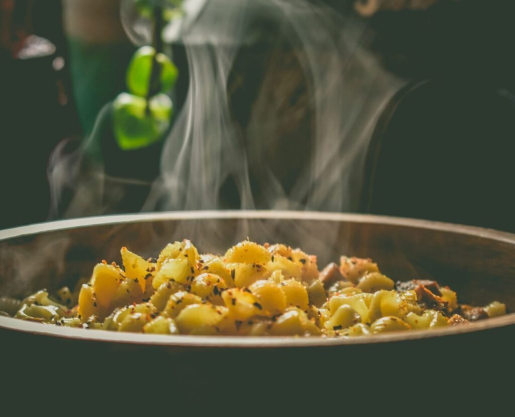 Big round bowl with aromatic pasta with herbs and vegetables smoking in soft light