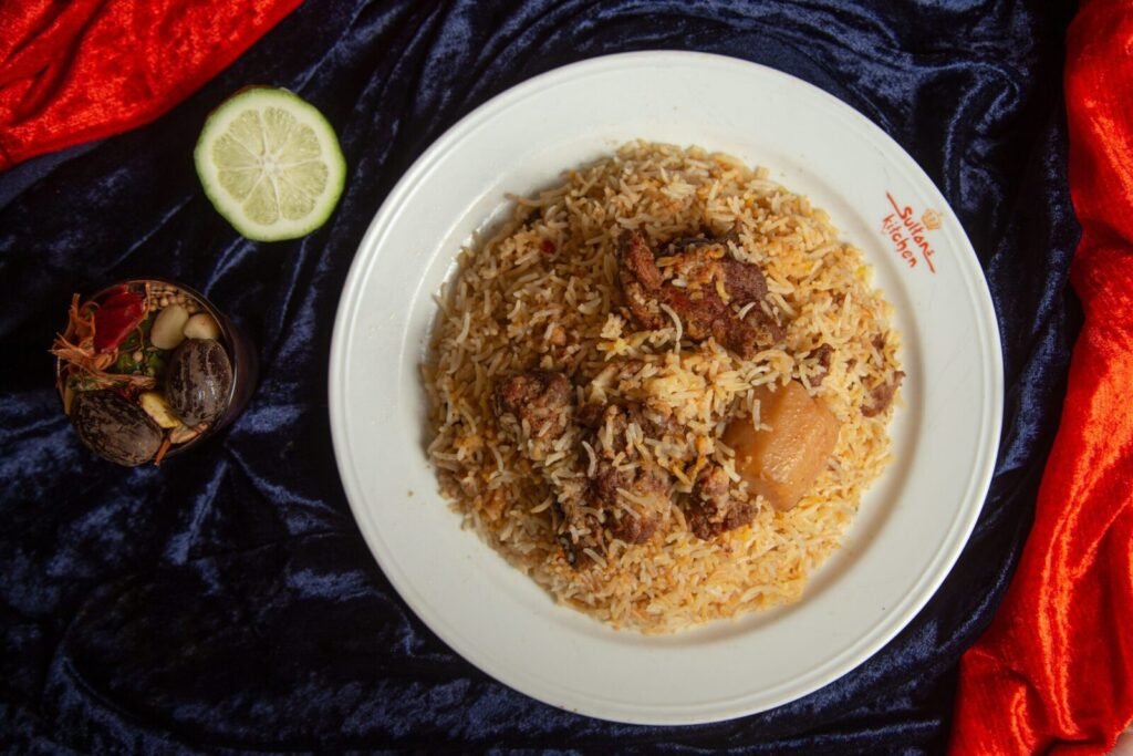 Delicious biryani with tender lamb pieces served on a white plate garnished with spices and lime.