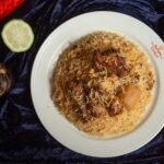 Delicious biryani with tender lamb pieces served on a white plate garnished with spices and lime.