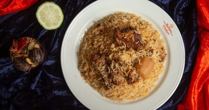 Delicious biryani with tender lamb pieces served on a white plate garnished with spices and lime.
