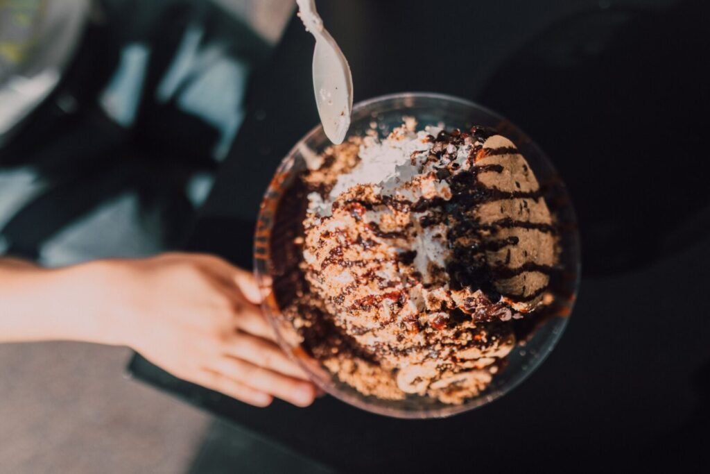 Flatlay of chocolate ice cream in a bowl with a spoon and hand reaching out.