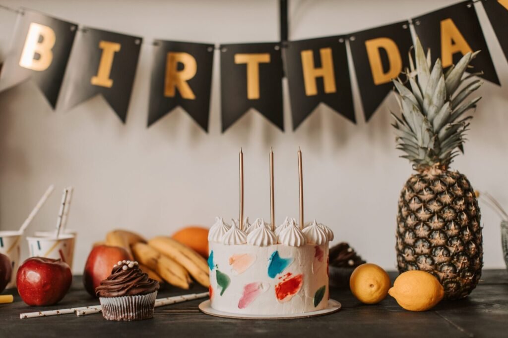 A colorful birthday cake with fruits and festive decorations on a table indoors.