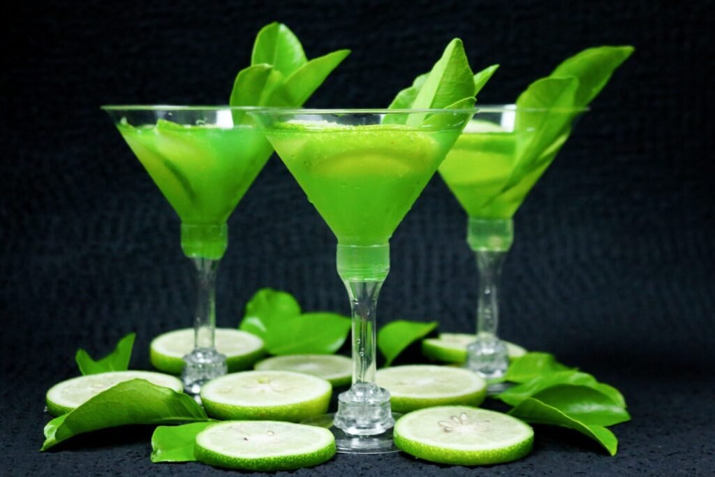 Three refreshing lime cocktails in martini glasses with green leaves on a black background.